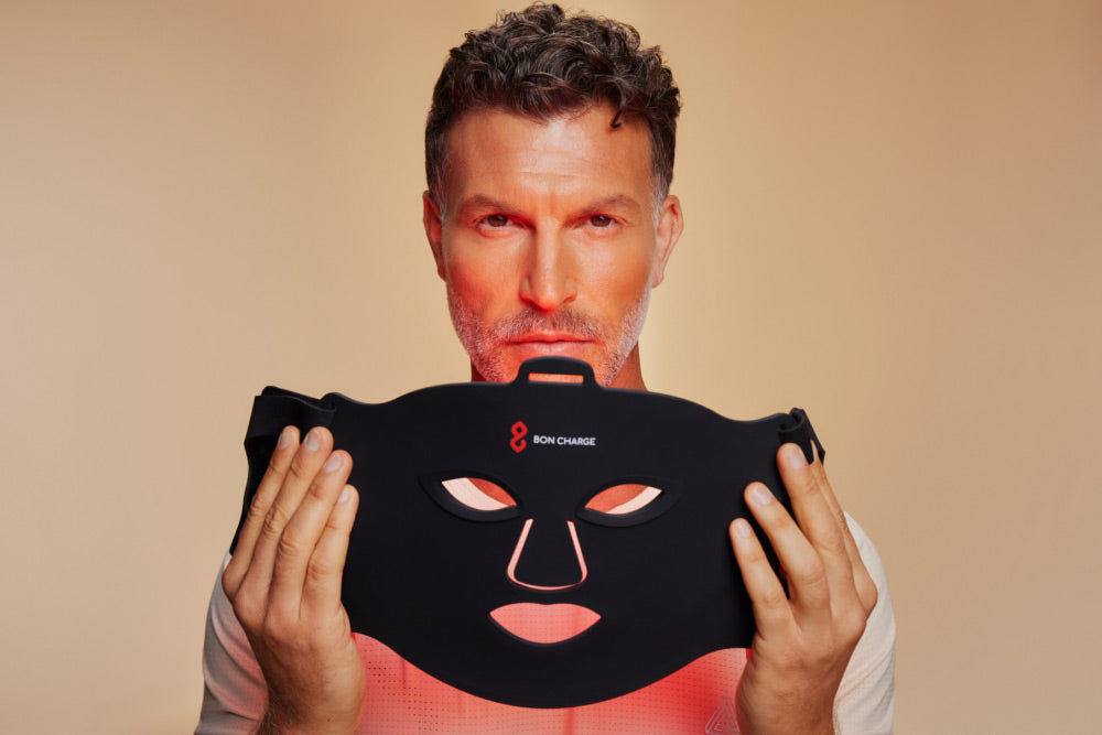 Man Holding Red Light Face Mask Towards Face